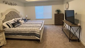 A bedroom with a bed, dresser, TV stand, and a window with blinds. - Beautiful 2022 Constructed Patio Home. Sleeps up to 6 people. 10mins DIA Airport (Commerce City)