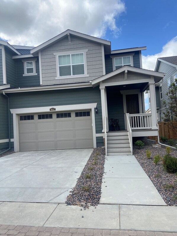 A two-story house with a garage, a front porch, and a small garden area. - Beautiful 2022 Constructed Patio Home. Sleeps up to 6 people. 10mins DIA Airport (Commerce City)