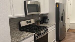 A modern kitchen with white cabinetry, a stainless steel stove, a microwave, and a refrigerator. - Beautiful 2022 Constructed Patio Home. Sleeps up to 6 people. 10mins DIA Airport (Commerce City)