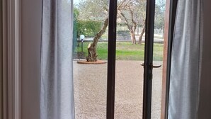 A room with a sliding glass door leading to an outdoor area with a gravel path and trees. - House of Olives (Lazise)