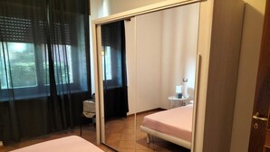 A bedroom with a bed, a small bedside table, a chair, and a wardrobe. - House of Olives (Lazise)