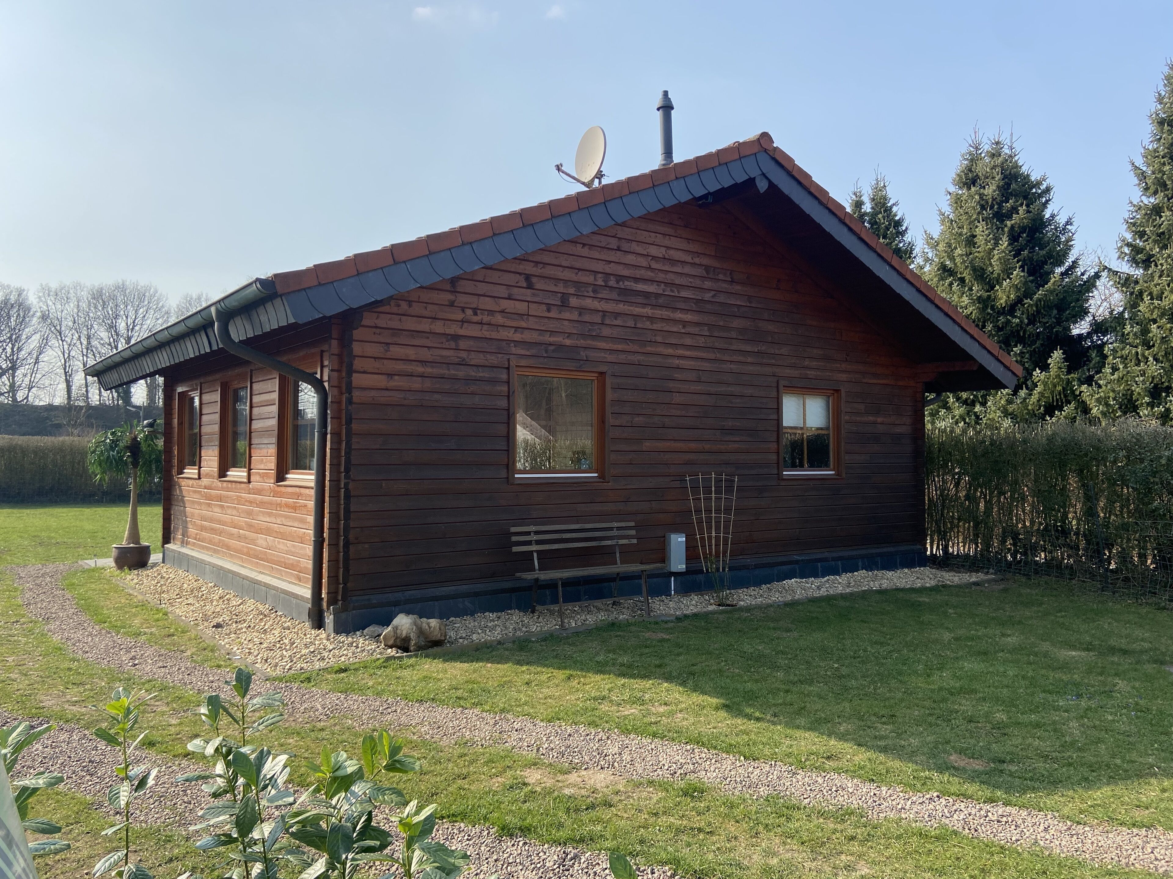 A wooden cabin with a sloped roof, a satellite dish, and a bench outside.