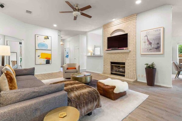 A modern living room with a fireplace, a ceiling fan, and artwork on the walls.
