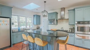 Een keuken met blauwe kastjes, een centraal eiland met krukken, een dakraam en een RVS afzuigkap.