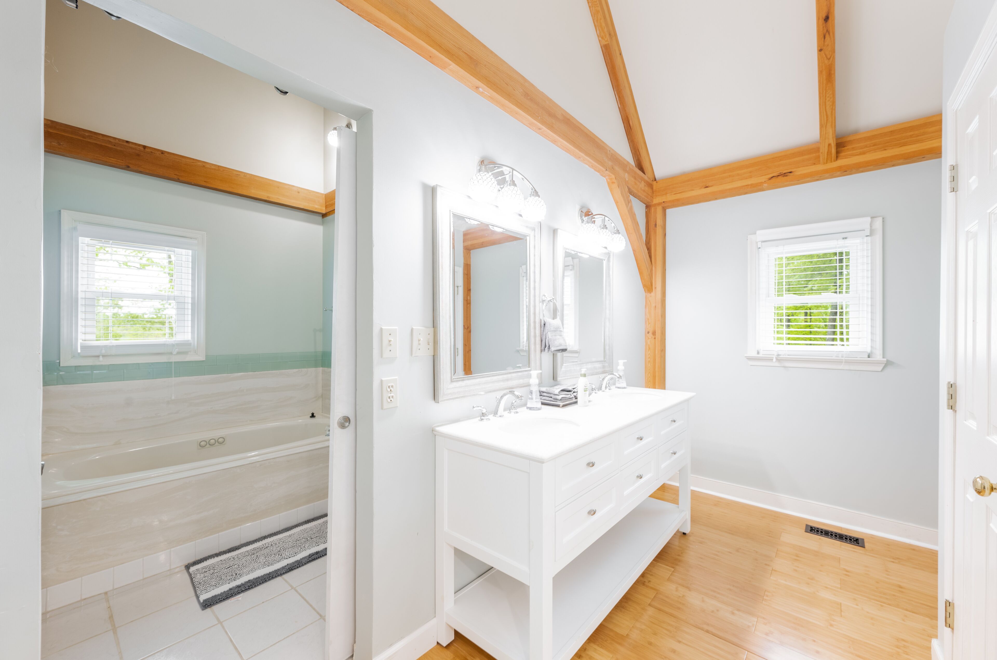 A bathroom with a white vanity, a large mirror, and wooden beams on the ceiling.