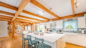 A spacious kitchen with wooden beams, white cabinets, and a large island with bar stools. - Beautiful and Private 6000 sqft waterfront home with private dock and hot tub! (Mineral)