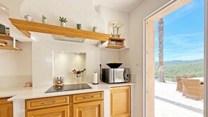 A kitchen with wooden cabinets, a microwave, and a view of a palm tree and chairs outside.