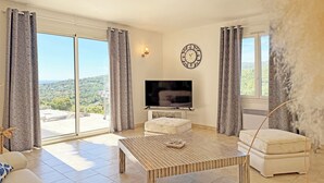 A spacious living room with a television, a sofa, a coffee table, and a view of the outdoors.