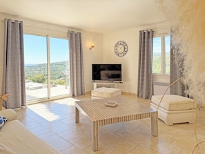 A spacious living room with a television, a sofa, a coffee table, and a view of the outdoors.