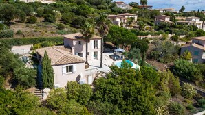 A Mediterranean-style villa with a swimming pool, surrounded by lush greenery and other residential buildings.