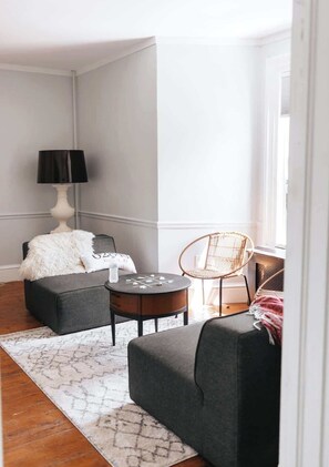 Un salon comprenant un canapé, un pouf, une table basse ronde et une lampe.