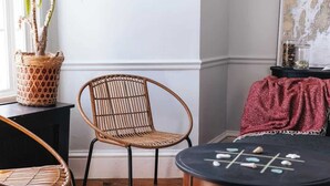 A cozy room with a wicker chair, a small round table with stones, a potted plant, and a map on the wall.