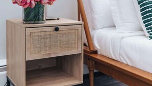A bed with a wooden headboard, a bedside table with a lamp and a vase of flowers, and a white pillow with a green striped pillow on a black floor.