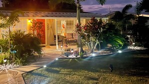 Un espacio exterior bien iluminado con una palmera, un sendero y un edificio con puerta roja.