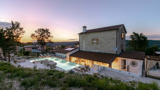 Ein zweistöckiges Steinhaus mit Swimmingpool, Sitzgelegenheiten im Freien und Blick auf einen malerischen Sonnenuntergang.