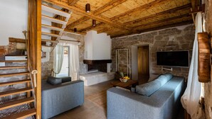 Ein rustikales Interieur mit einer Steinwand, Holzbalkendecke, Kamin, Fernseher und einer Treppe.
