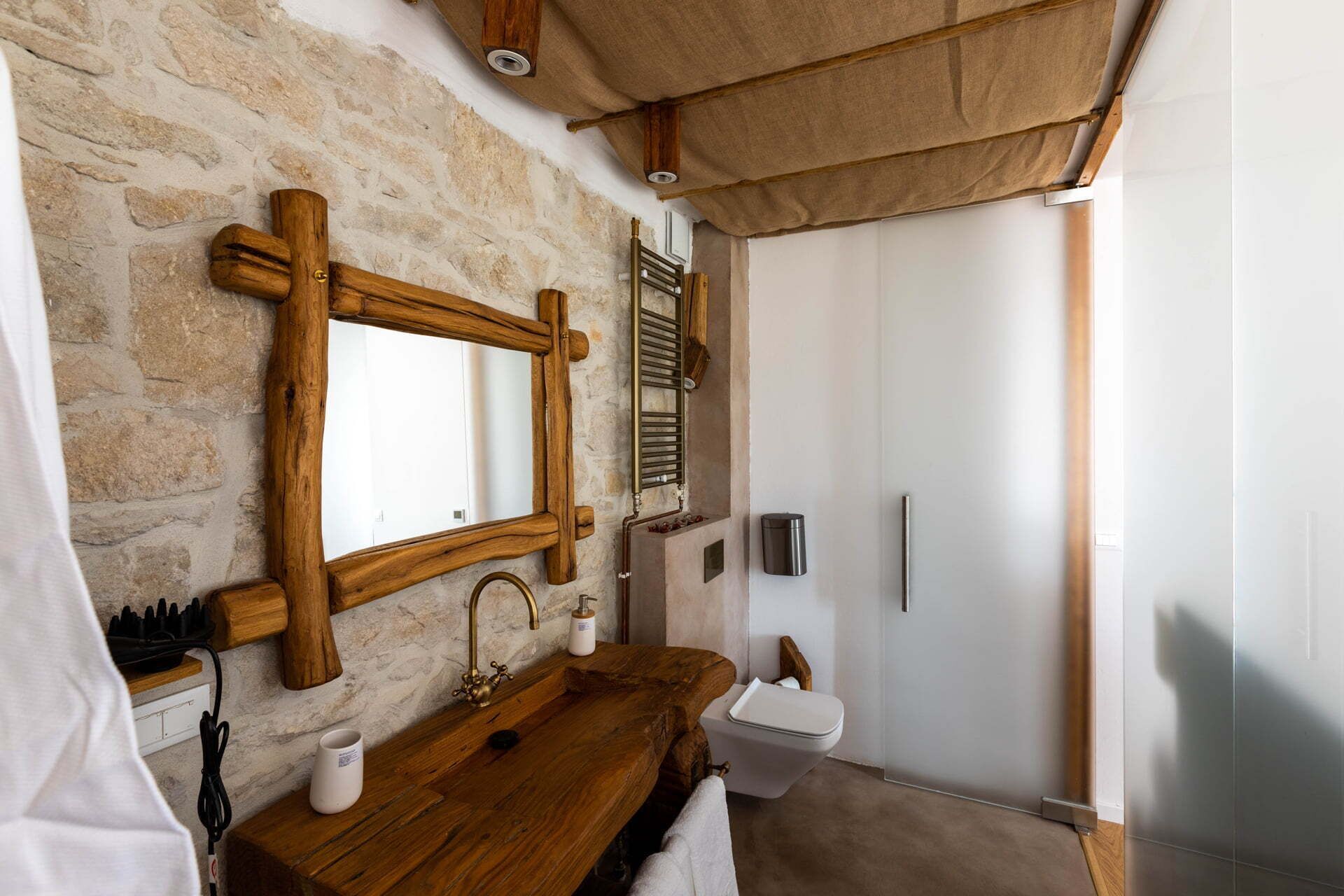 A bathroom with a stone wall, wooden vanity, a large mirror, a shower with a glass door, and a towel rack.