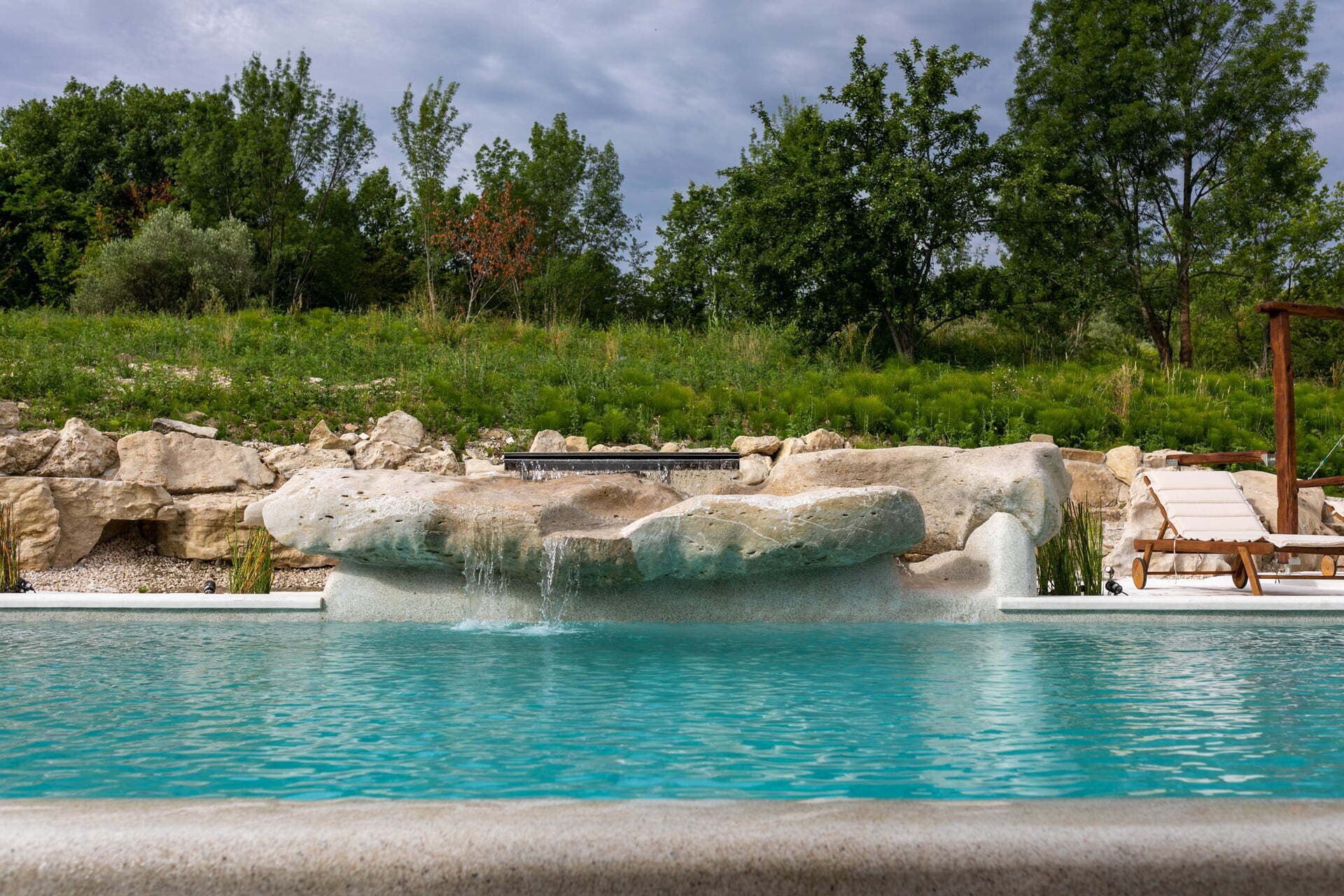 A swimming pool with a waterfall feature, surrounded by rocks and greenery.