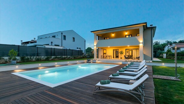 Et moderne hus med to etager, en swimmingpool og et udendørs siddeområde.