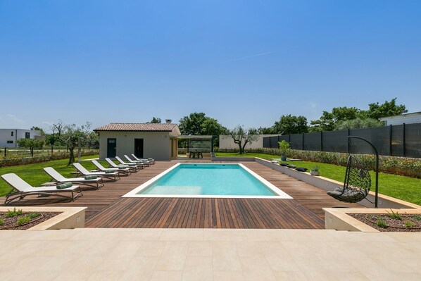 A rectangular swimming pool with a wooden deck, surrounded by lounge chairs and a small building. - Villa Charm with Pool (Nova Vas)