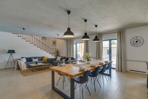 Sala moderna com mesa de jantar de madeira, cadeiras pretas, uma escada e vista para o exterior.