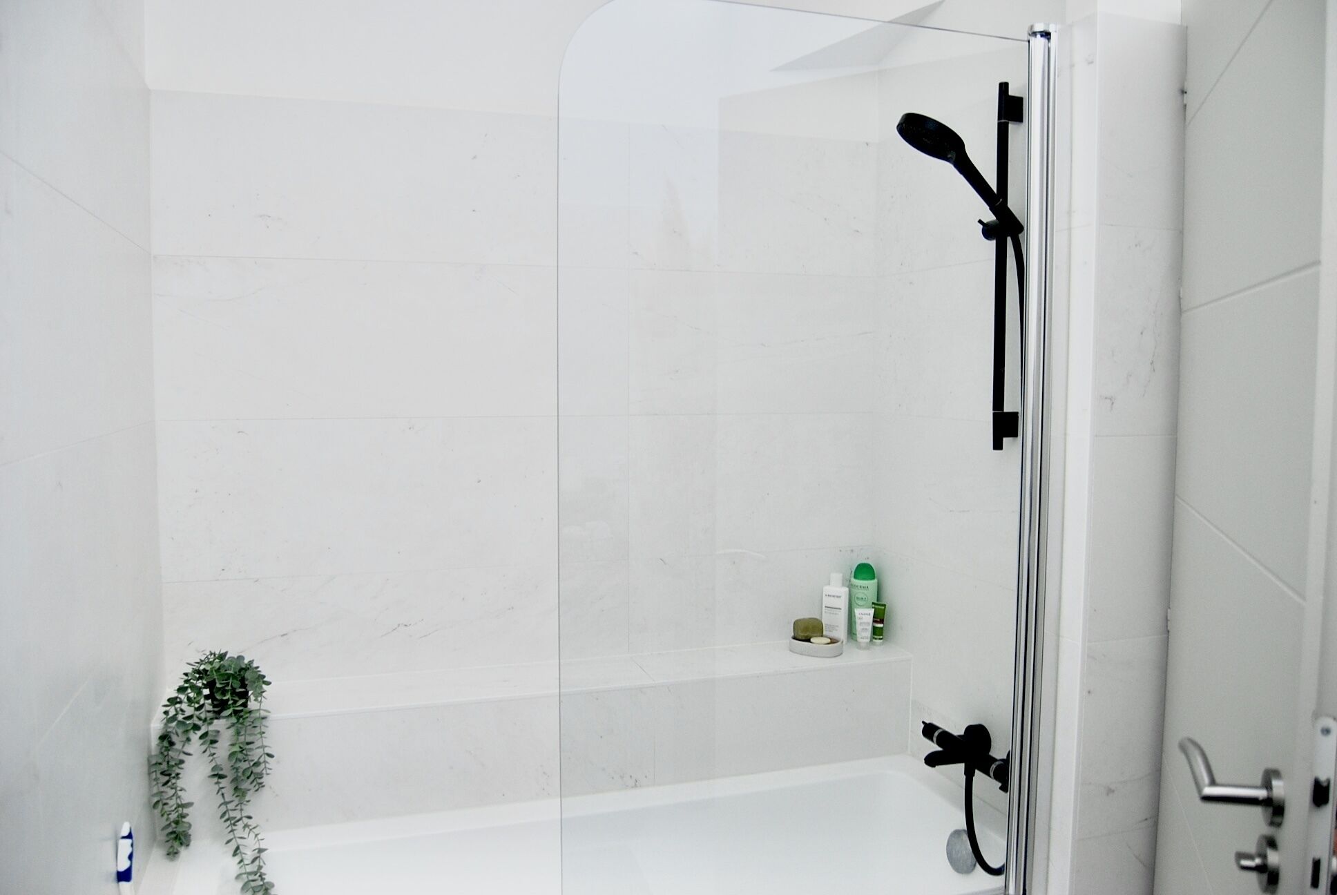 A modern shower enclosure with a glass door, a handheld showerhead, and a wall-mounted control.