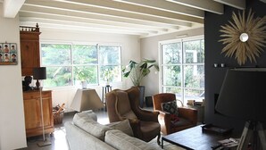 A living room with a sofa, armchairs, a coffee table, and a fireplace. There are large windows providing natural light and views of greenery outside. - Villa (ST NAZAIRE)