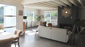 A spacious living room with a fireplace, large windows, and a high ceiling with exposed beams. - Villa (ST NAZAIRE)