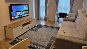 Ein modernes Wohnzimmer mit Flachbildfernseher, einer Couch, einem Schreibtisch und einem kleinen Tisch.
