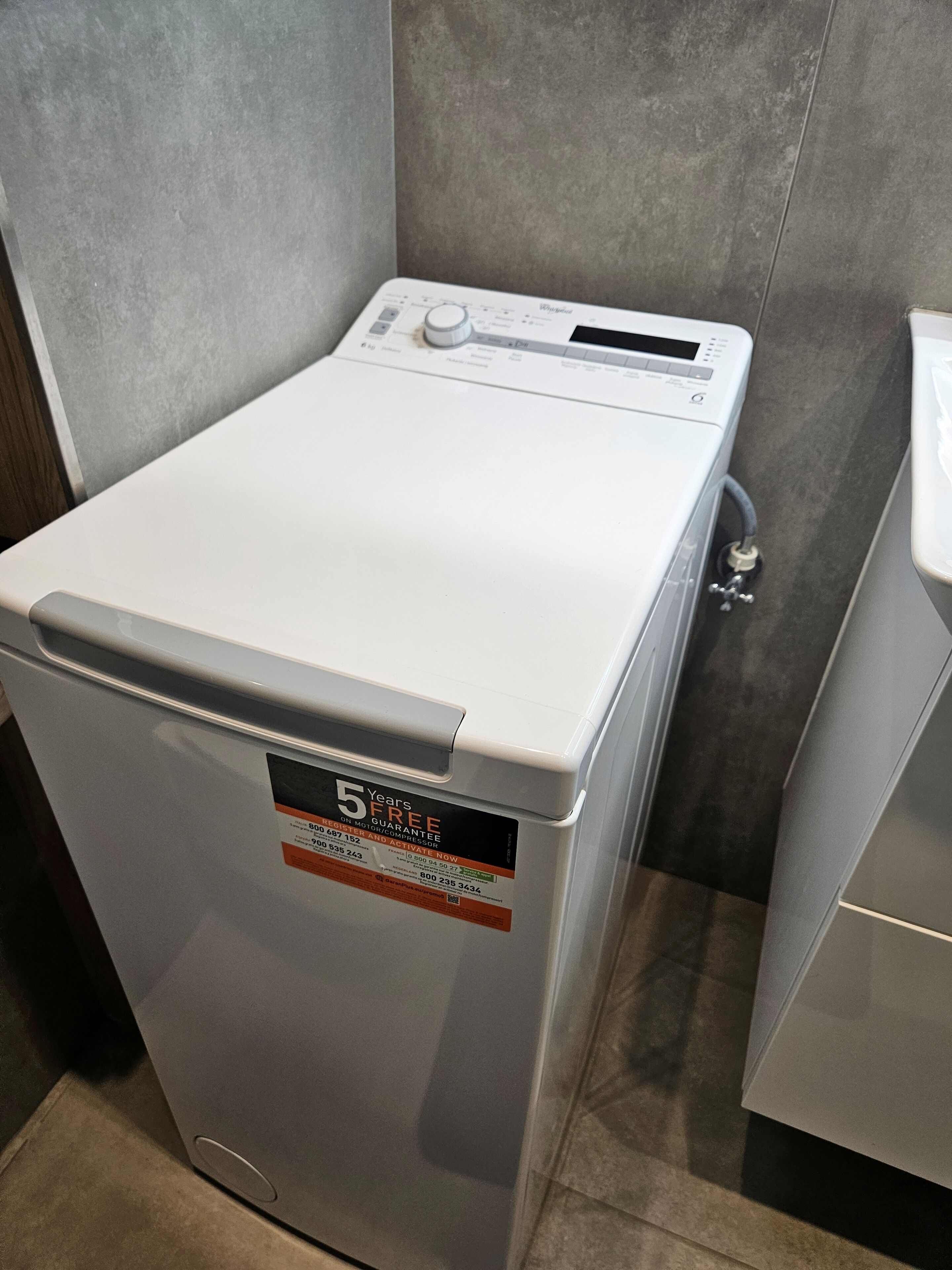 A compact, white, front-loading washing machine with a control panel and a 5-year free service guarantee sticker.