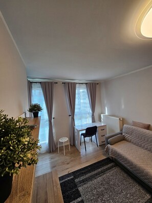 Una habitación moderna y bien iluminada con un escritorio de madera, una silla negra, un sofá y un radiador.
