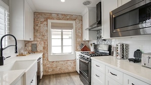 A modern kitchen with white cabinetry, a brick accent wall, a large window, stainless steel appliances, and a microwave. - ❤️of PHX in Historic Willo • Heated Pool • Chef's Kitchen • Fast WiFi (Phoenix)