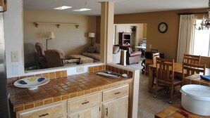 A kitchen with a tiled backsplash, wooden cabinets, and a dining area with a table and chairs. - Lakefront Home fully furnished (Sun Lakes)