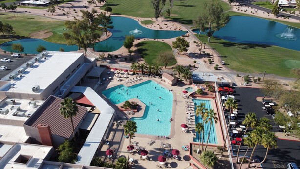 An aerial view of a resort with multiple swimming pools, a golf course, and a large building with air conditioning units. - Lakefront Home fully furnished (Sun Lakes)