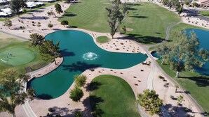 An aerial view of a golf course with a central pond, sand bunkers, and a bridge. - Lakefront Home fully furnished (Sun Lakes)
