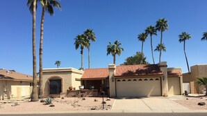 A residential area with a house featuring a red-tiled roof, a garage, and a front yard with palm trees. - Lakefront Home fully furnished (Sun Lakes)