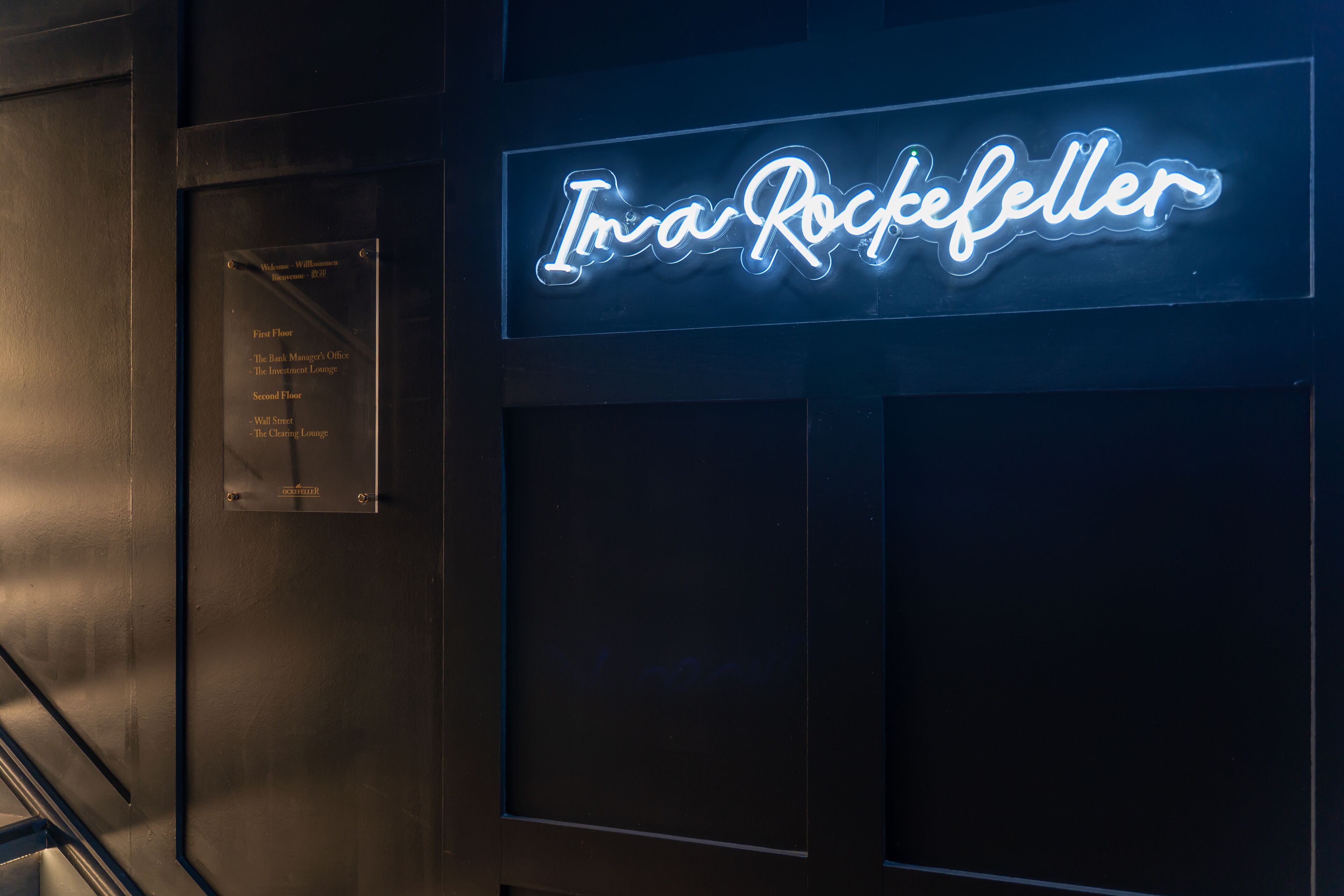 A neon sign reading "In a Rockefeller" on a dark wall.