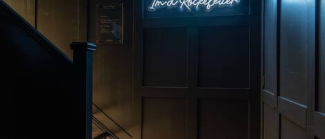 Un escalier menant à une porte sur laquelle est apposée une enseigne au néon avec l’inscription : « Je suis un Rockefeller. »