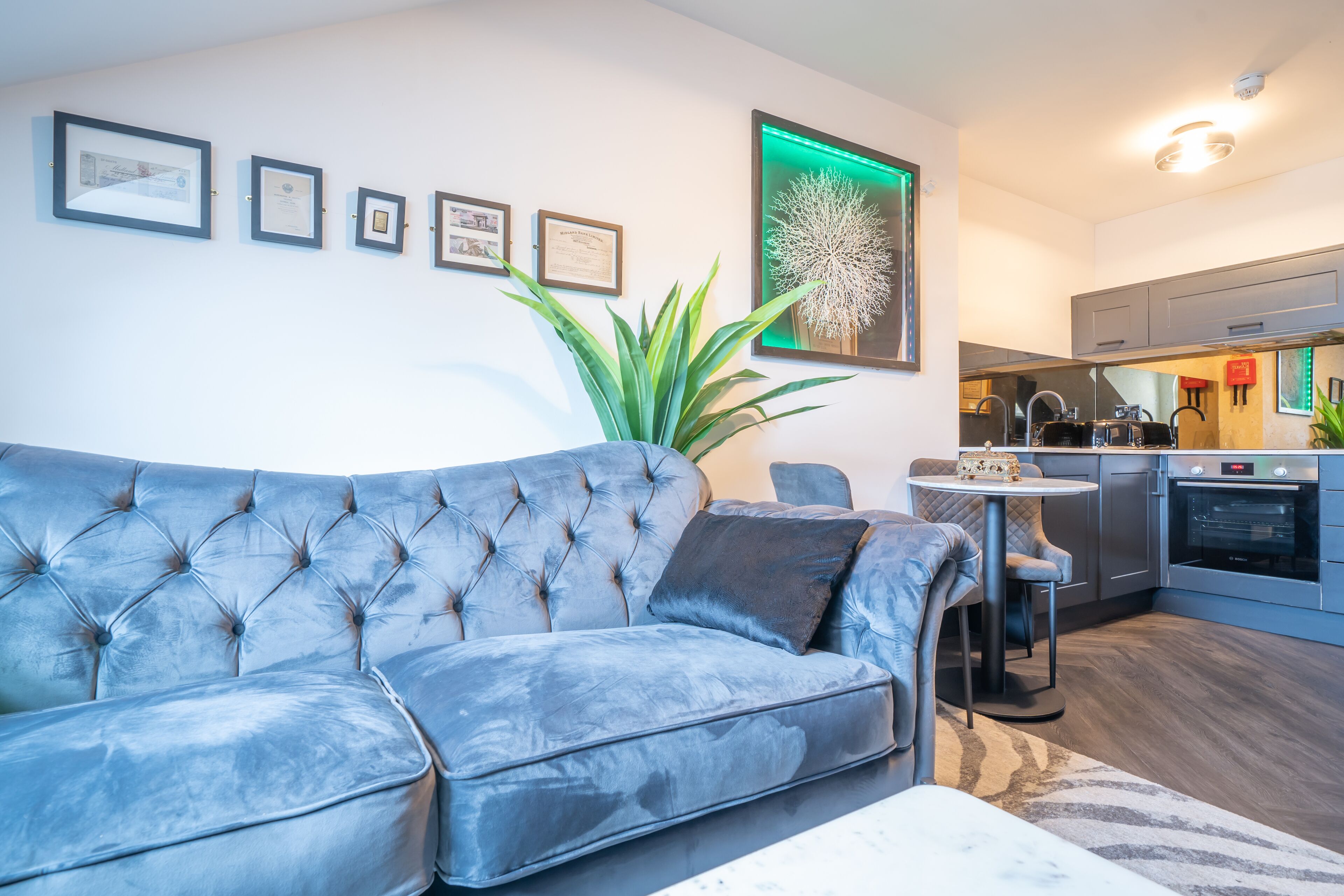 A modern living room with a tufted sofa, a dining table, and a kitchen area with stainless steel appliances.