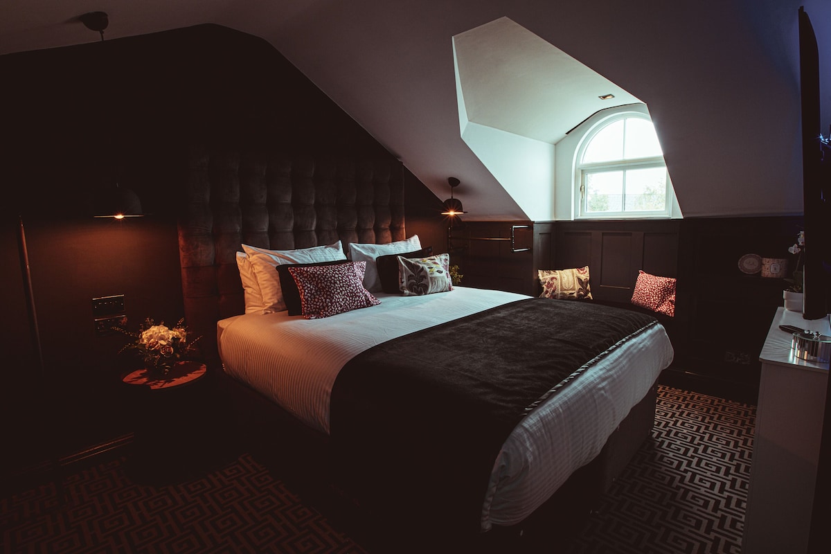 A bedroom with a large bed, a dark headboard, and a skylight.