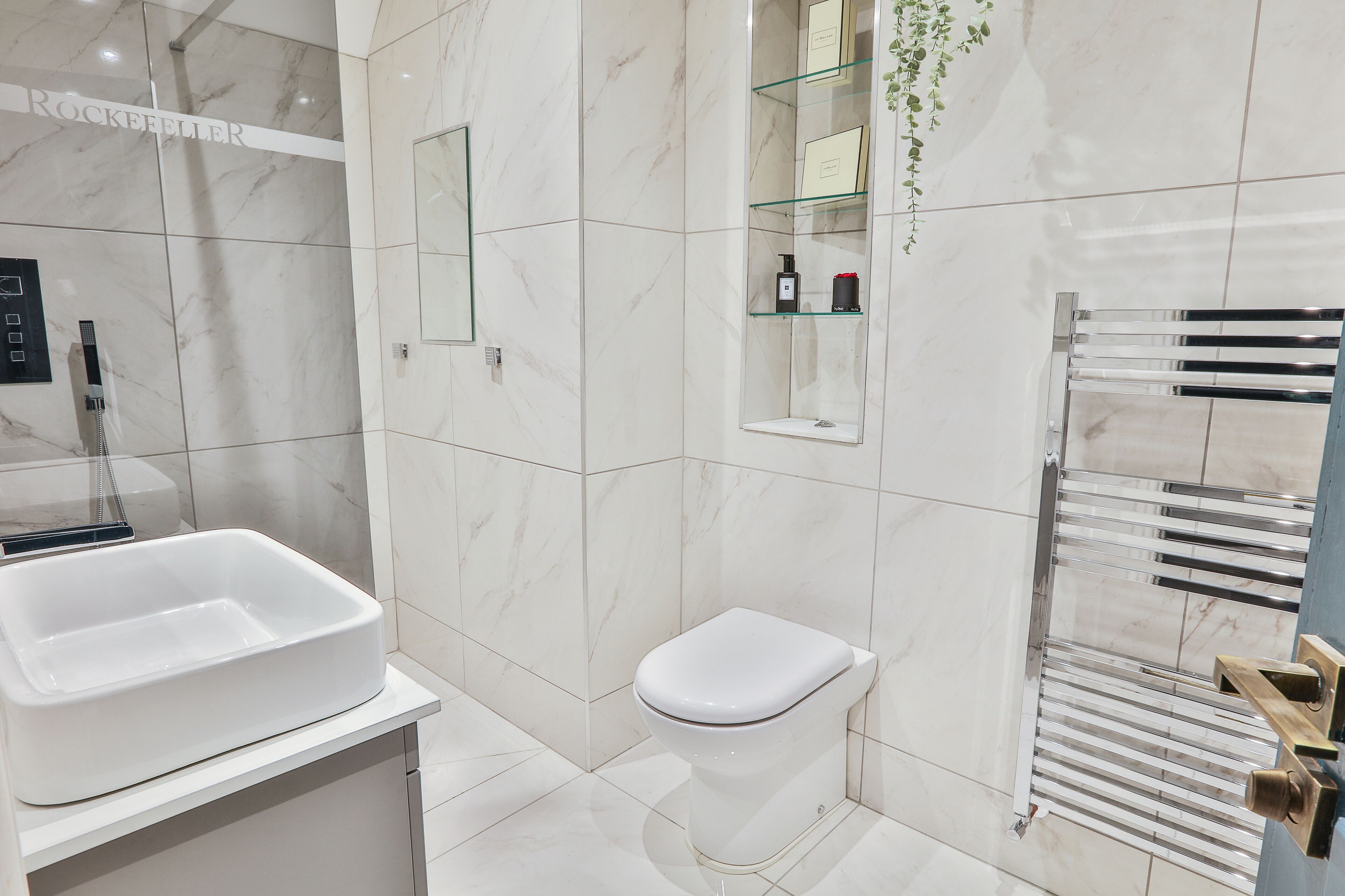 A modern bathroom with a white sink, toilet, and a glass shelf with toiletries.