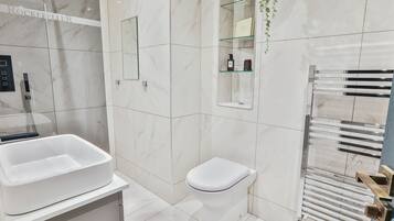 A modern bathroom with a white sink, toilet, and a glass shelf with toiletries.