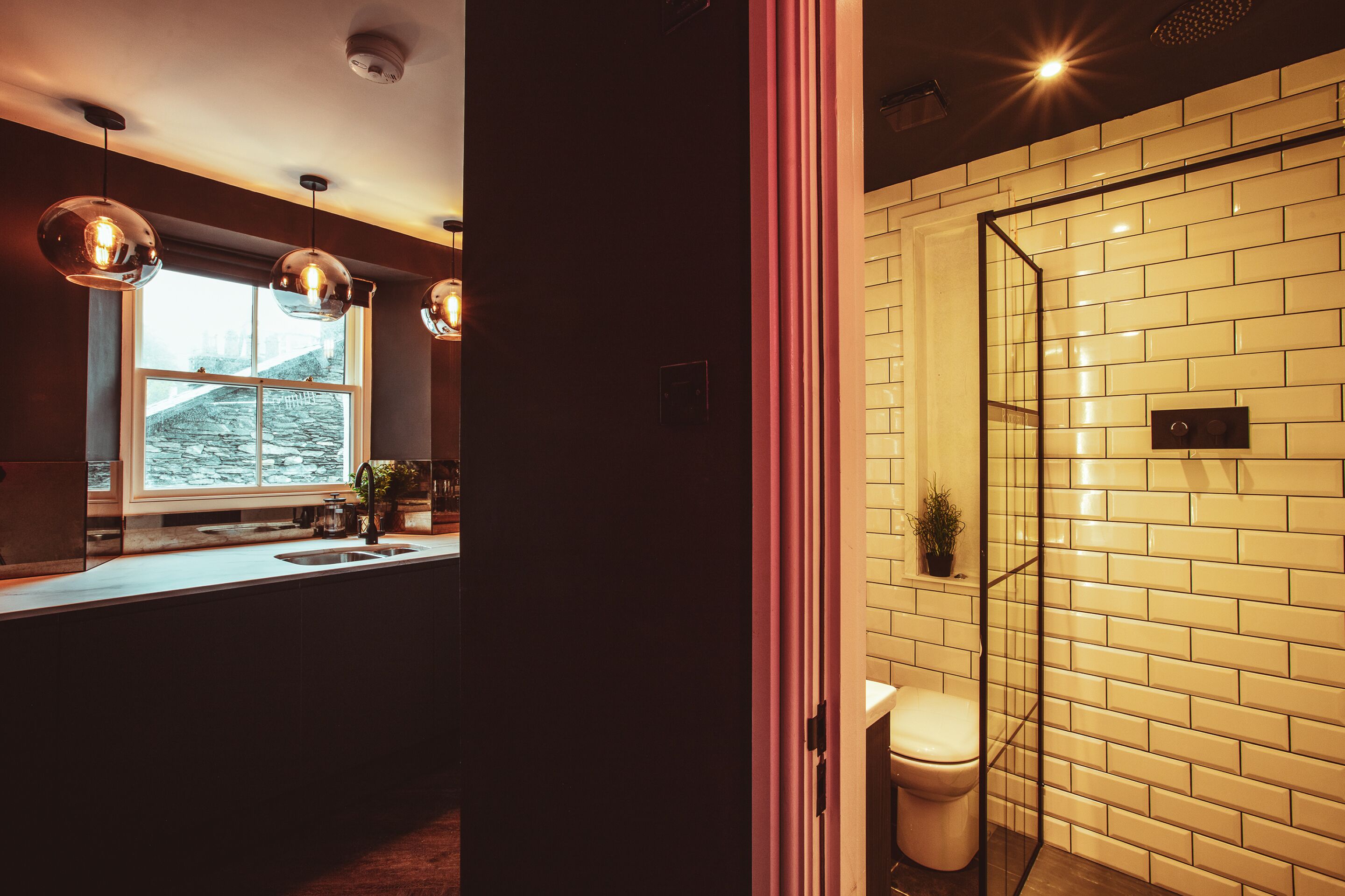 Une salle de bain moderne avec une douche à l’italienne en verre, un mur recouvert de carreaux blancs et des luminaires suspendus.