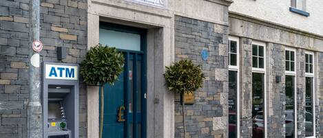 A building with a stone facade, a blue door, an ATM, and two potted plants.