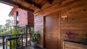 A wooden cabin with a balcony, a door marked with the number 2, and a small table with chairs.