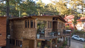A two-story wooden cabin with a balcony, a stone foundation, and a car parked in front.