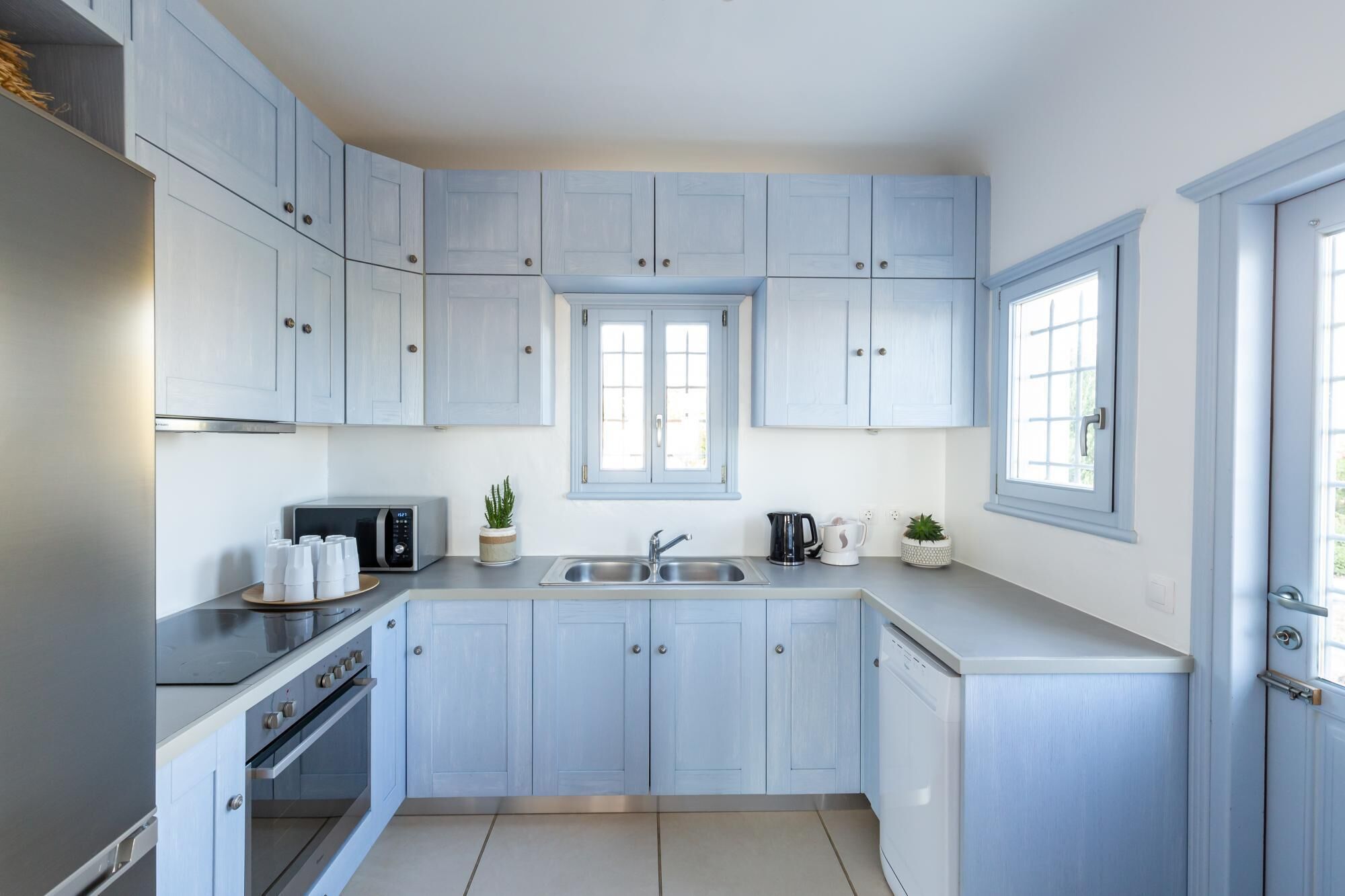 Una cuina moderna amb armaris de blau clar, un frigorífic d'acer inoxidable, un forn encastrat, un microones i un rentaplat.