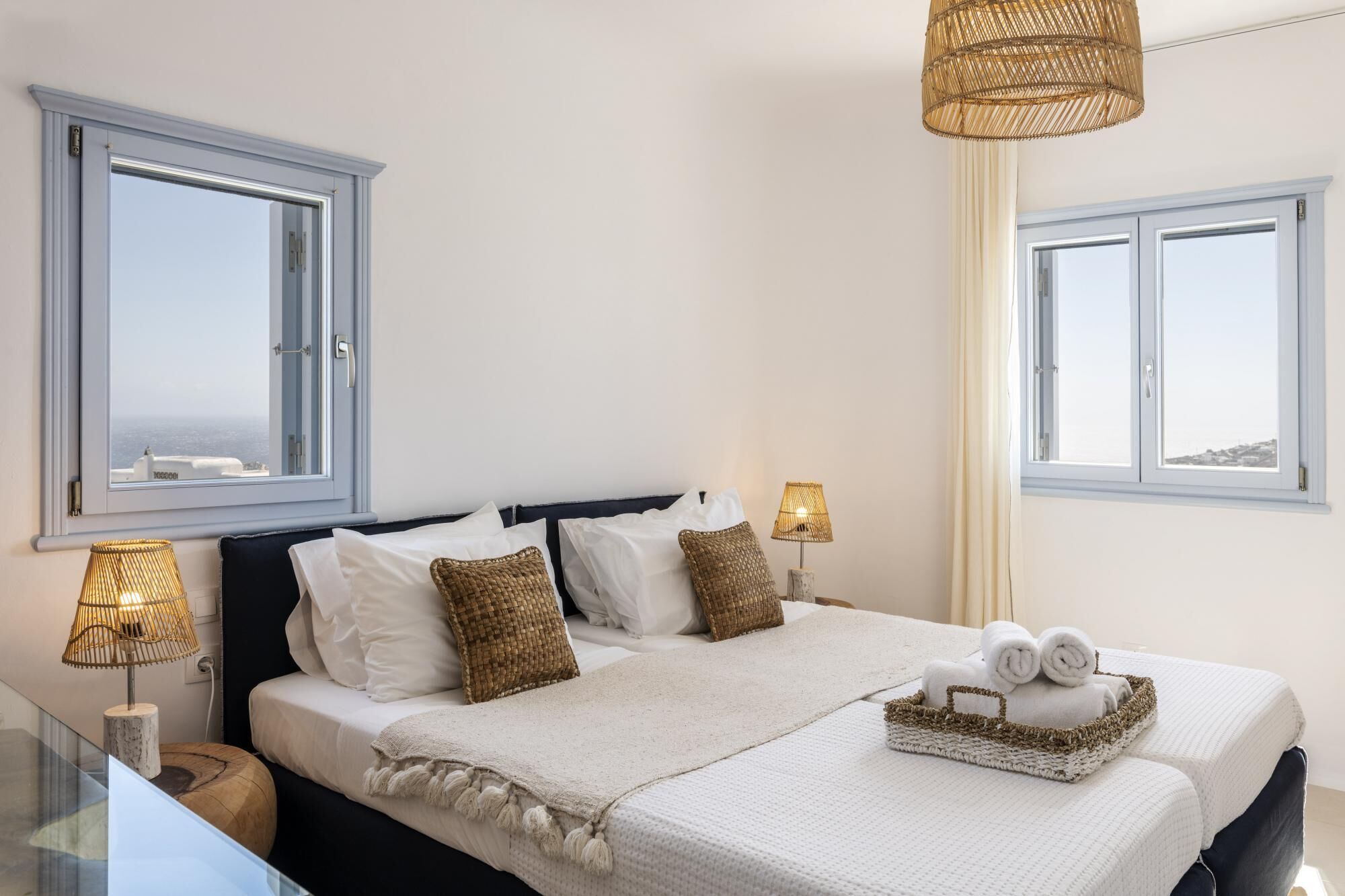 A bedroom with a large bed, two bedside lamps, a window with a view, and a small table with a lamp.