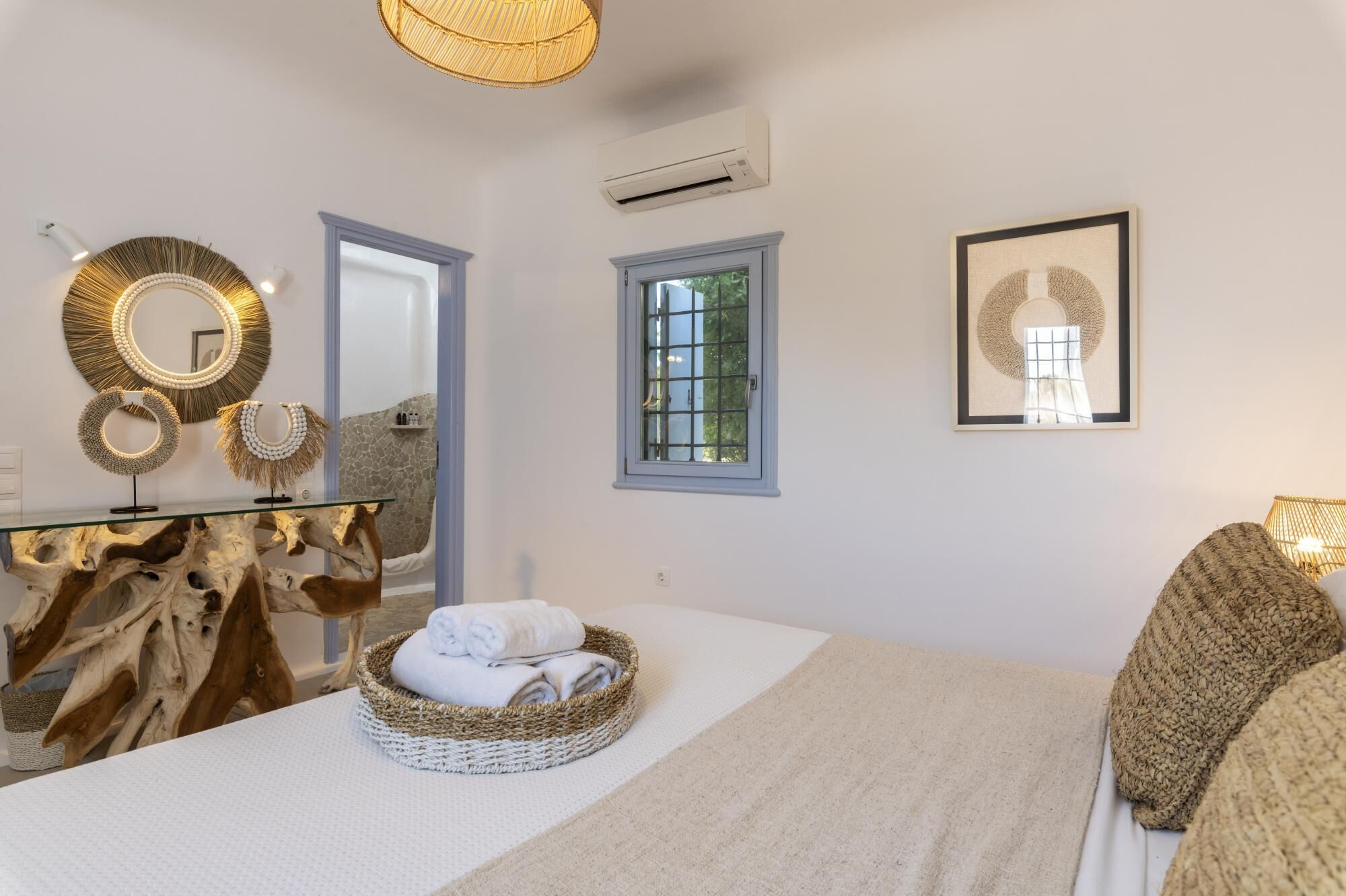 Quarto com uma cama grande, uma mesa de vidro com objetos decorativos, uma janela e um ar condicionado.