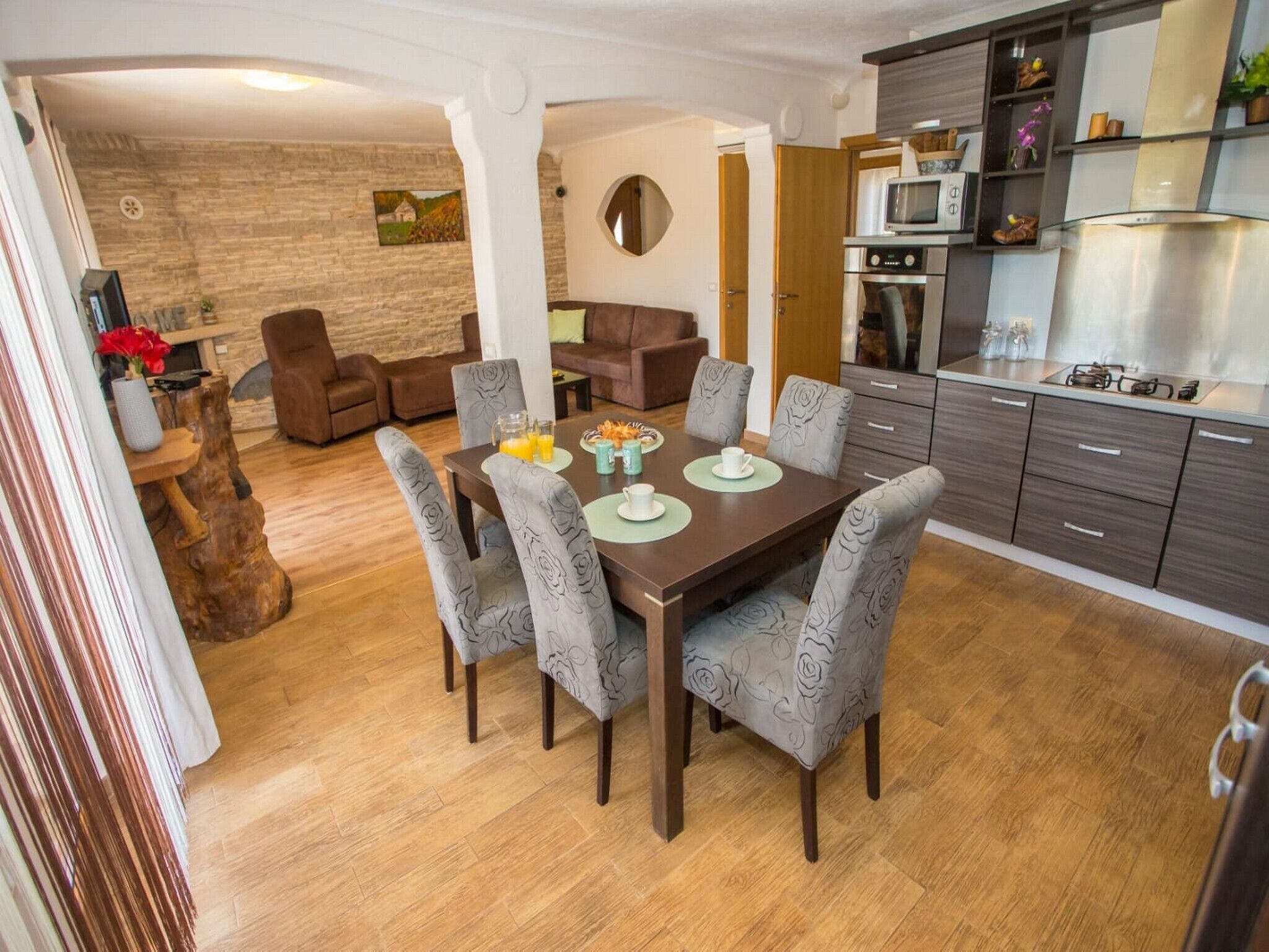 Eine moderne Küche mit Essbereich, mit einem Holztisch, grau gepolsterten Stühlen und einer Steinwand mit einem Gemälde.